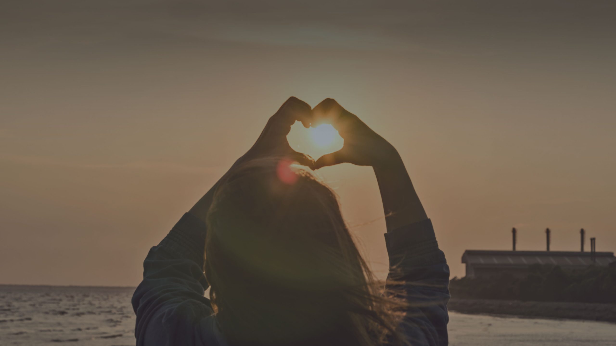 Child forming a heart with her hands in the sunset